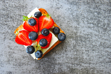 Healthy toasts with white cheese, fresh strawberries and blueberries. The concept of a healthy snack or lunch. 