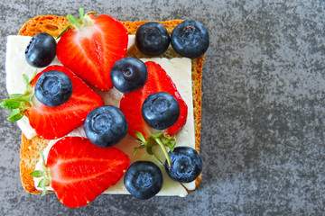Healthy toasts with white cheese, fresh strawberries and blueberries. The concept of a healthy snack or lunch. 