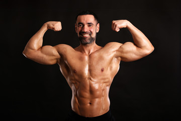 Fototapeta premium muscular man flexing his muscles on black background and smiling 