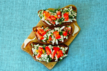 Toasts with white cheese and herbs with garlic on a small wooden board. Open sandwiches with selenium and cottage cheese. Garlic toast with grated mozzarella cheese and greens. 