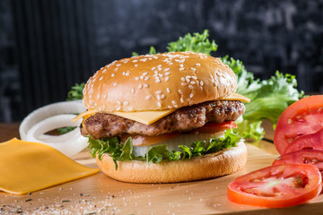 Cheese burger with ingredients on wooden platter