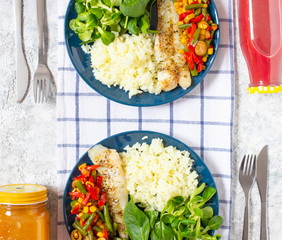 Healthy lunch for two people. Baked fish, rice, fresh spinach, lettuce, cherry tomatoes, baked fresh vegetables, a bottle of grapefruit fresh and a bottle of cherry and apple fresh