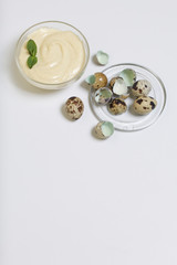 Handmade mayonnaise using quail eggs. In a glass container, decorated with greenery. Near quail eggs and shell from them. On a white background.