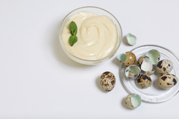 Handmade mayonnaise using quail eggs. In a glass container, decorated with greenery. Near quail eggs and shell from them. On a white background.