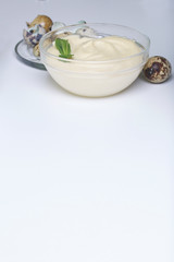 Handmade mayonnaise using quail eggs. In a glass container, decorated with greenery. Near quail eggs and shell from them. On a white background.
