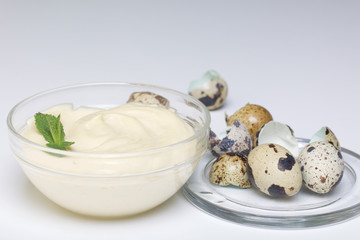 Obraz na płótnie Canvas Handmade mayonnaise using quail eggs. In a glass container, decorated with greenery. Near quail eggs and shell from them. On a white background.