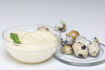Handmade mayonnaise using quail eggs. In a glass container, decorated with greenery. Near quail eggs and shell from them. On a white background.