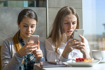  two beautiful girls in a cafe write sms on a smartphone, in the hands of the phone