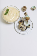 Handmade mayonnaise using quail eggs. In a glass container, decorated with greenery. Near quail eggs and shell from them. On a white background.