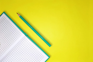 Green notebook and pencil on yellow background