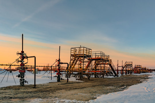 Oil production wells are located in a row at an oil field in western Siberia. Sunset spring sunny day.