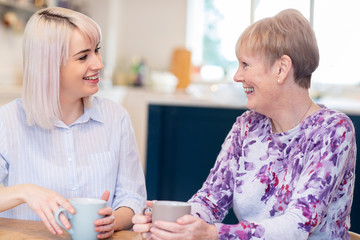 Young Woman Taking Time To Visit Senior Female Neighbor And Talk