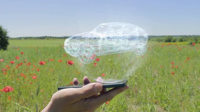 Hologram of Suv car on a smartphone. Person activates holographic image on the phone screen on the field with blooming poppies