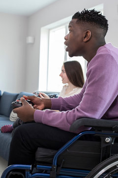 Teenage Boy In Wheelchair Playing Computer Video Game With Freind At Home