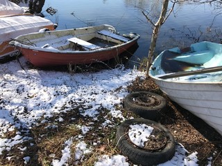 Small boats on land during winter. Old car tires. - 256650446