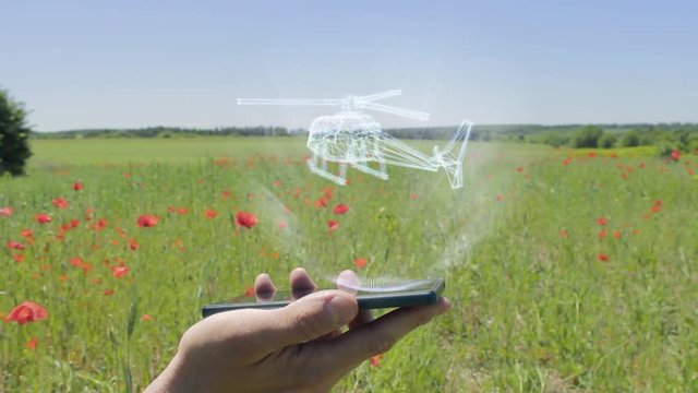 Hologram of helicopter on a smartphone. Person activates holographic image on the phone screen on the field with blooming poppies