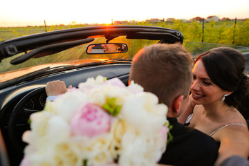 Beautiful wedding couple watching the sunset in a convertible car.