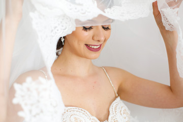 A brunette bride with a veil smiles at the camera