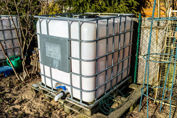 Large industrial liquid tank with a capacity of 1000 liters, 265 gallons with a metal protective grille. Placed in a home garden as a rainwater tank