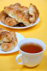croissants on a white plate with a Cup of tea on a yellow background