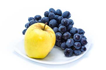 Blue grapes with yellow apple on a white plate.