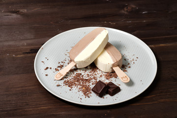 white chocolate ice cream on a stick on a white plate with chocolate chips on the dack wood background