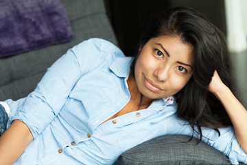 Young Latin woman smiling and relaxing on a sofa. Home