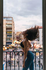 Side view of slim brunette lady with windy hair standing on balcony with view on city street.