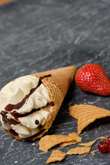 vanilla ice cream in waffle cone with chocolate icing on dark grey background with strawberry