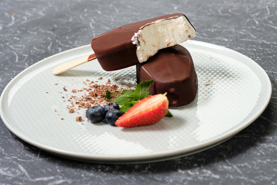 Chocolate-coated ice cream with strawberries and blueberries on a white plate close-up