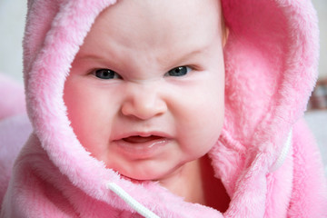 Portrait of a little very bad girl baby. She is dressed in a pink fluffy blouse with a hood. She has an aggressive facial expression. Funny girl.