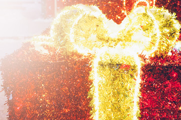 Big red neon gift box with a yellow bow at the evening festive festival. Amazing light. Close-up