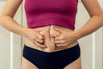 Chubby woman hand holding her own belly fat at outdoor under the sunlight