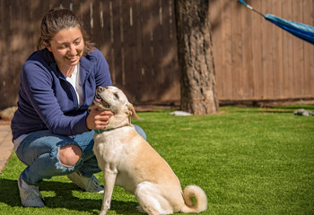 Pretty girl petting a happy white dog with a curly tail in a backyard with a hammock in the background.