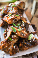 Close-up of crispy baked chicken wings, glazed with honey sauce with fresh scallions on wooden background 