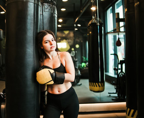 Tired fit woman resting after training near heavy bag at boxing room. Female boxer relaxing after workout