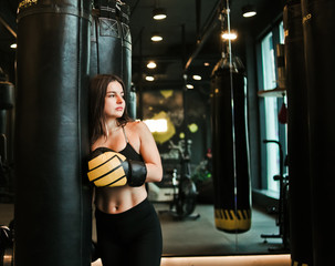 Fototapeta na wymiar Tired fit woman resting after training near heavy bag at boxing room. Female boxer relaxing after workout