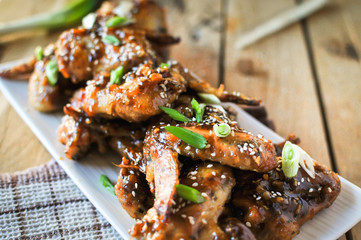 Close-up of crispy baked chicken wings, glazed with honey sauce with fresh scallions on wooden...