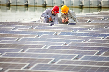 Two Asian senior engineers are doing research and development in front of the photovoltaic panels floating on the water surface.