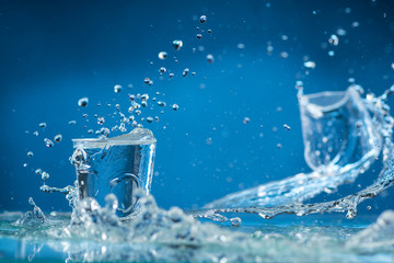 Naklejka na ściany i meble falling small glasses and spilling water on a blue background