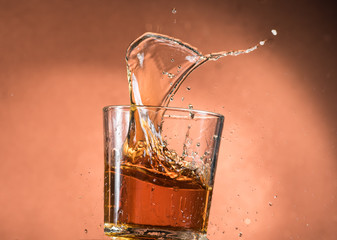 splash in a glass of whiskey with ice on an orange brown background