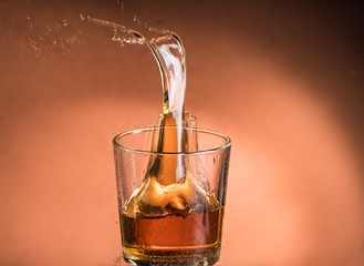 splash in a glass of whiskey with ice on an orange brown background