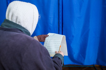 Obraz premium Illustrative image of the election in a democratic society. Elections in Ukraine Voting at a polling station. The elderly woman's voter gets acquainted with the contents of the ballot papers.