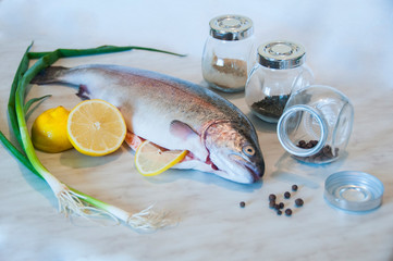 Raw trout with slices of lemon, pepper peas and pepper mill on a marble background. Fresh fish...