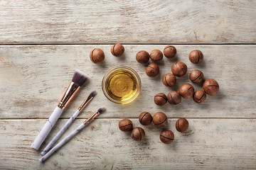 Bowl with oil, macadamia nuts and brushes on wooden table