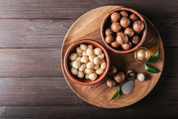 Bowls with macadamia nuts and oil on wooden table - obrazy, fototapety, plakaty