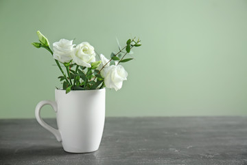 Cup with beautiful flowers on grey table