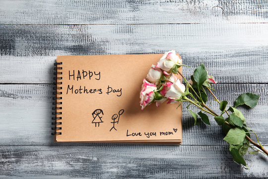 Notebook with greeting for mother and flowers on wooden background