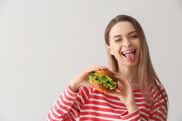 Beautiful happy young woman with tasty burger on light background