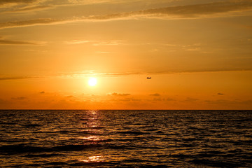 Fototapeta premium Golden, Fiery sunset on the Black Sea, on the beach. Coast, stones, waves, sun, beautiful sky, clouds. August, Batumi, Georgia. Water, ease, game. plane in the sky, tourism
